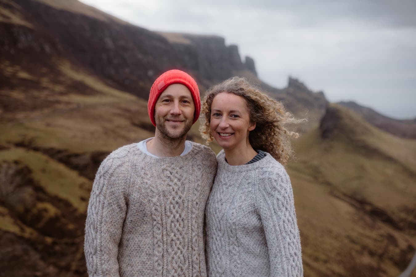 Oli and Steph smile at the camera wearing woollen jumpers at the Quiraing, Isle of Skye