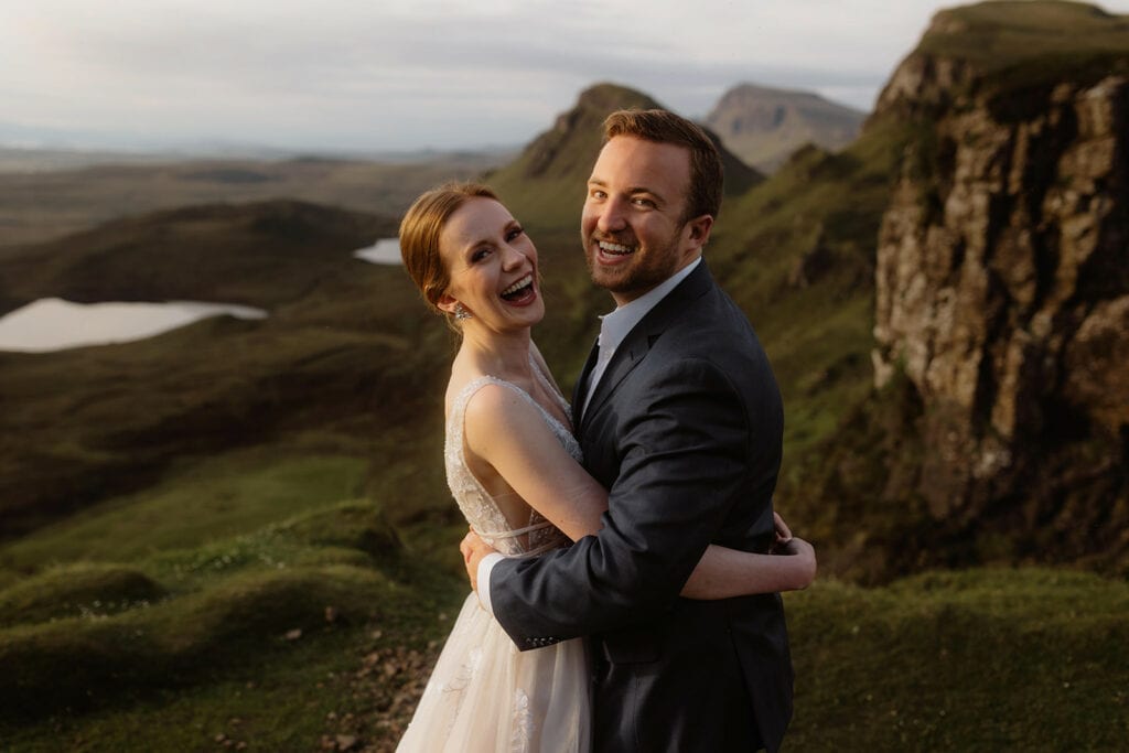 Celeste and Doug are embracing with big smiles in front of the stunning Quiraing, Isle of Skye, in the background.