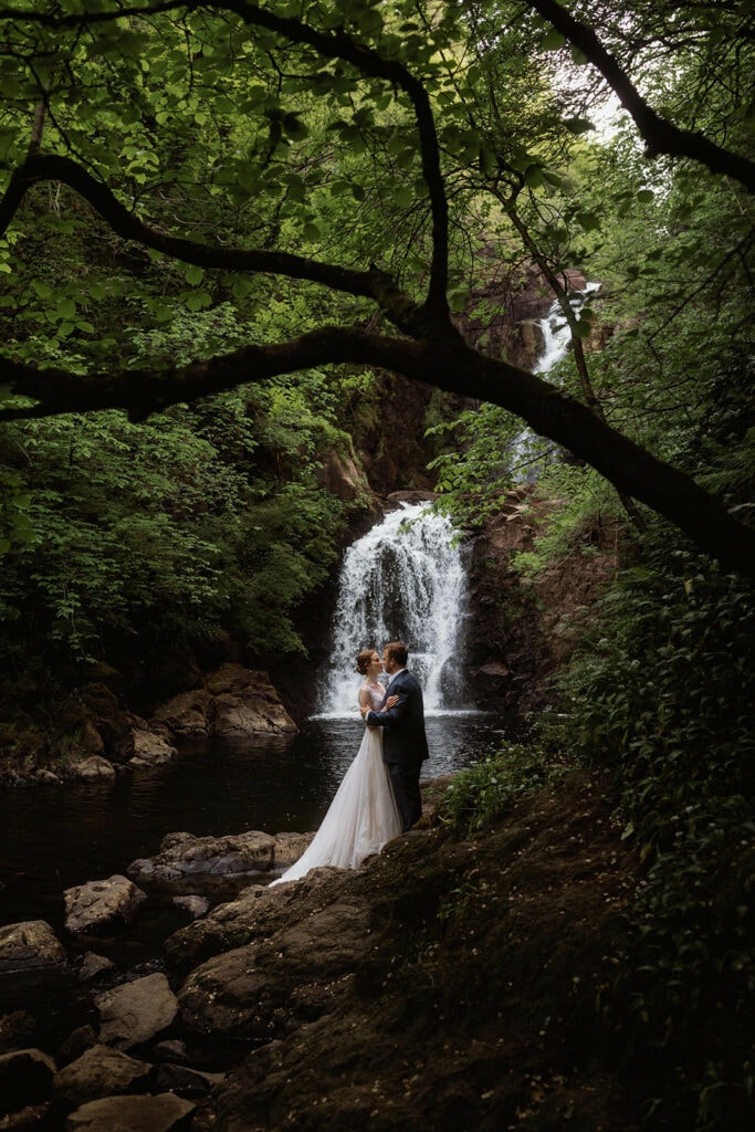 Celeste and Doug are smiling at each other with a backdrop of waterfalls cascading down in the background for their Scotland Post-Wedding photo session.