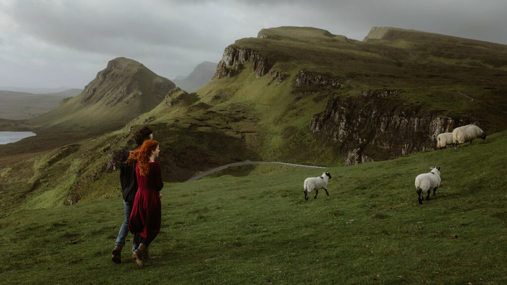 Ashley and Bobby walking through the picturesque Isle of Skye with sheeps in the background.